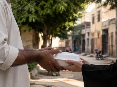 A box of food being handed from one person to another on a Lahore street